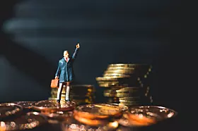 Figur im Anzug und mit Aktenkoffer, die auf Münzstapel steht und den Arm hebt