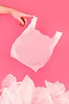 Hand die Plastiktüte hält vor rosa Hintergrund, auf dem Boden weitere Plastiktüten