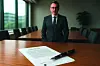 Ein Mann steht vor einem großen Schreibtisch, auf dem ein Vertrag und ein Füllfederhalter liegen.