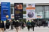 Menschenmenge vor einer Messehalle, an der Plakate mit den Aufschriften We are Intralogistics Pioneers und Logimat angebracht sind
