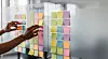 Hand verschiebt farbige Haftnotizen auf einem Kanban-Board mit Spalten To Do, In Progress und Done.