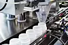 filling and packaging machine at pharmaceutical factory fills white plastic jars with tablets or ampoules containing dietary supplements. containers are lined up on conveyor belt.