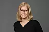 Frau mit Brille und blondem Haar vor grauem Hintergrund.